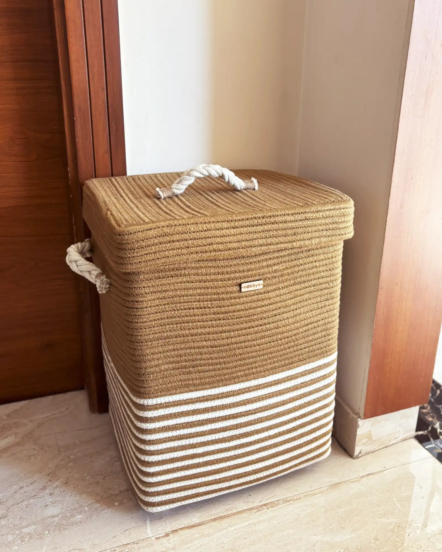 Brown and beige striped laundry basket with a handle on a wooden floor.